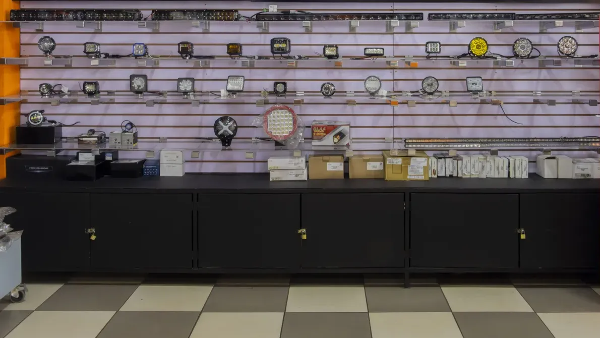 Pared de exhibición en la tienda Repuestos Alto con barras LED y luces de trabajo sobre paneles ranurados, encima de gabinetes negros.